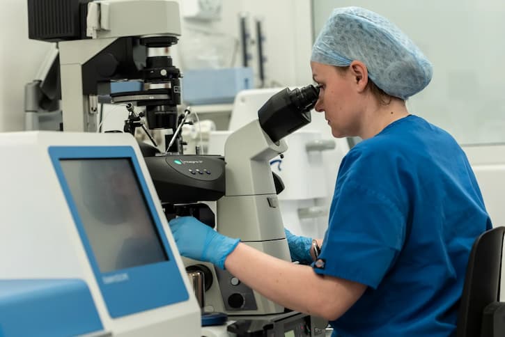 Embryologist looking through a microscope next to a computer