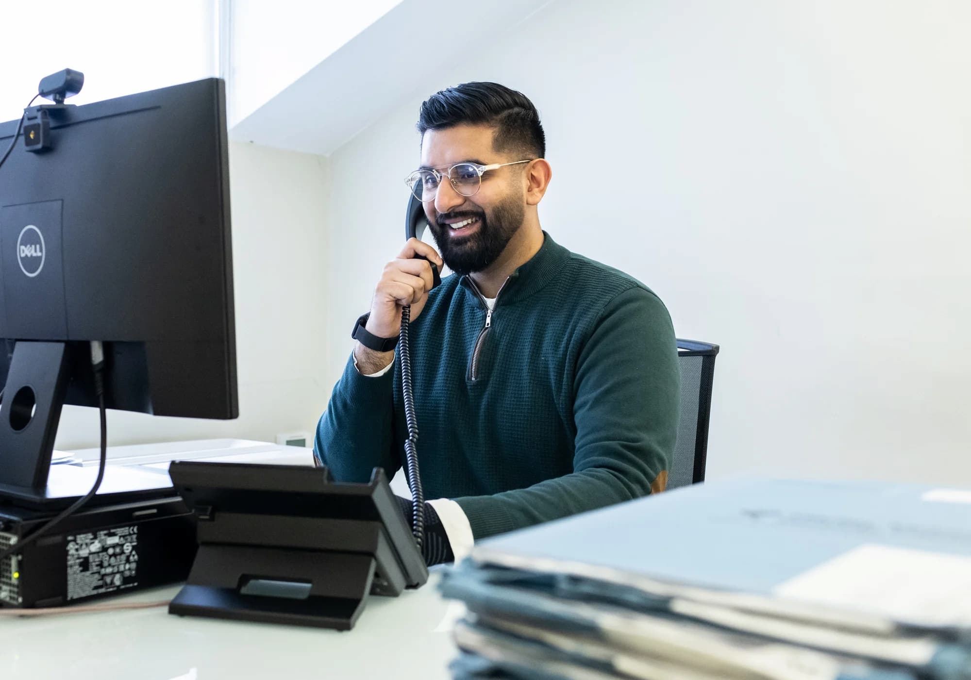 Male patient coordinator talking on a phone sitting in front of a computer