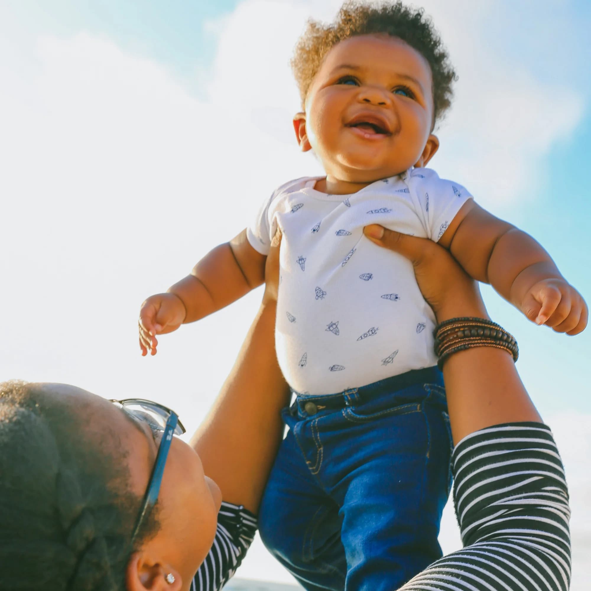 Black baby being held up high by a woman with glasses