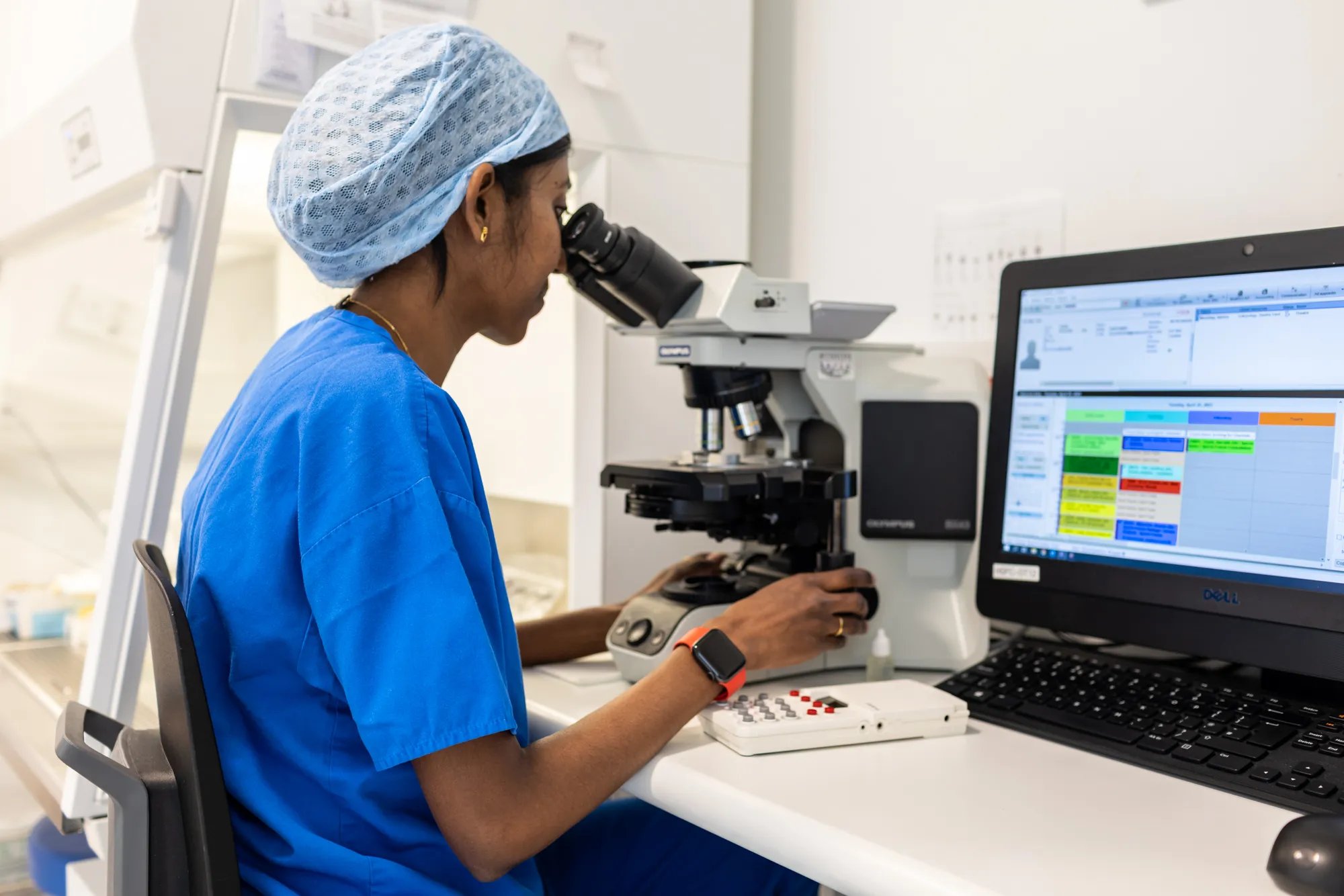 Embryologist dressed in scrubs, looking though a microscope.