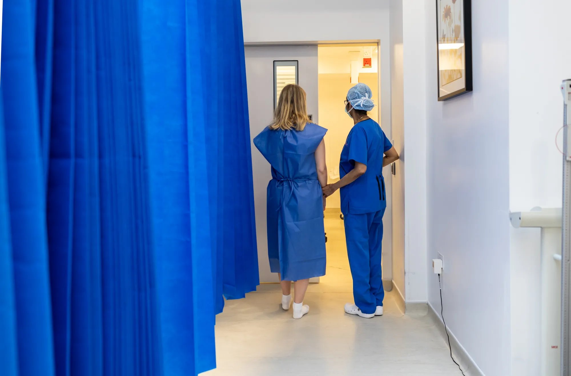 Patient wearing scrubs and a fertility doctor walking towards the door, theatre curtain taking the left side of the picture.