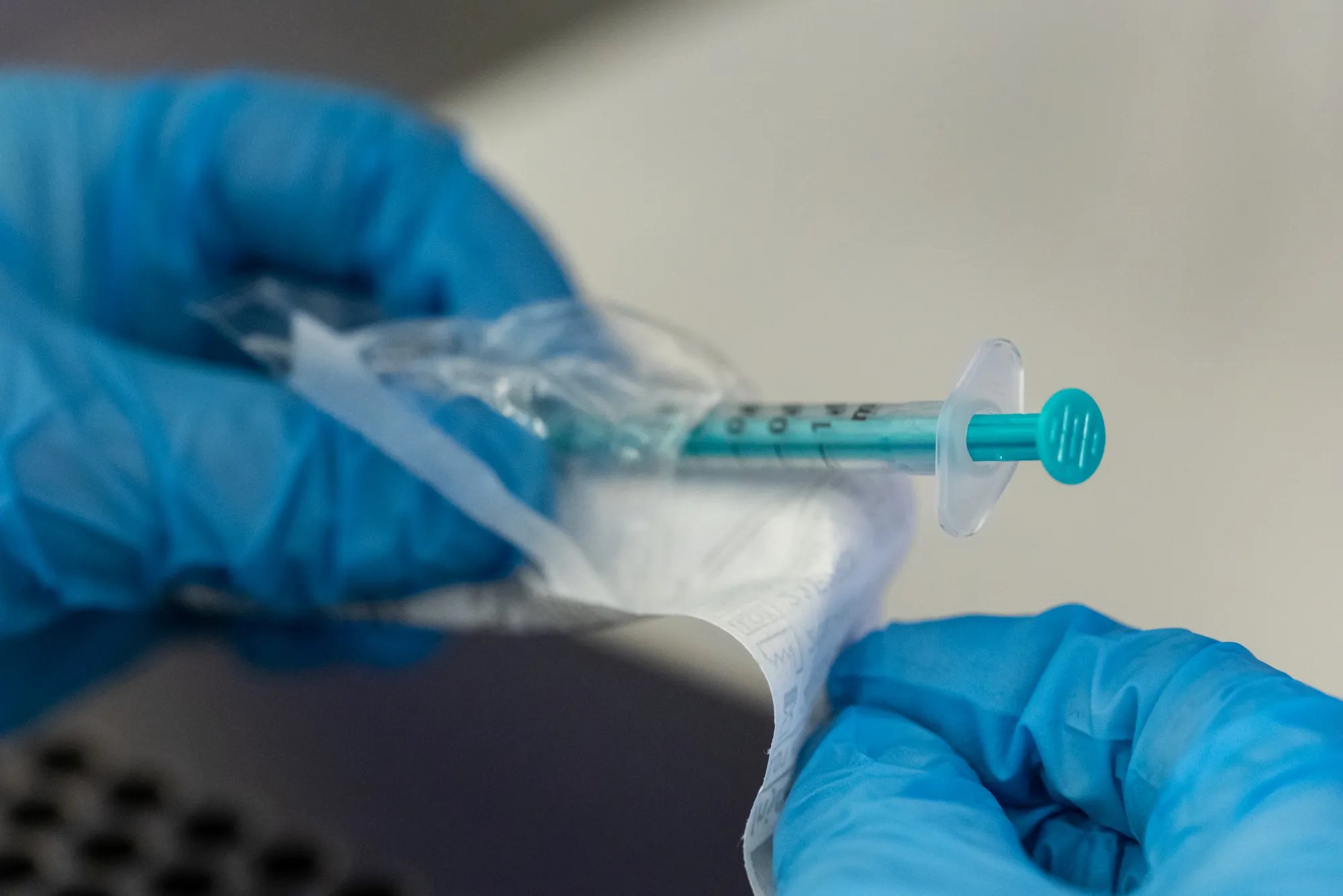 A syringe half in a package, held by a gloved hand, used to trigger ovulation.