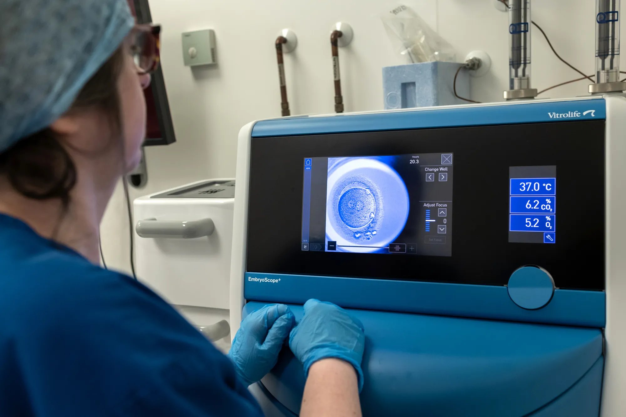 Embryologist dressed in scrubs, looking at a computer screen displaying an embryo.